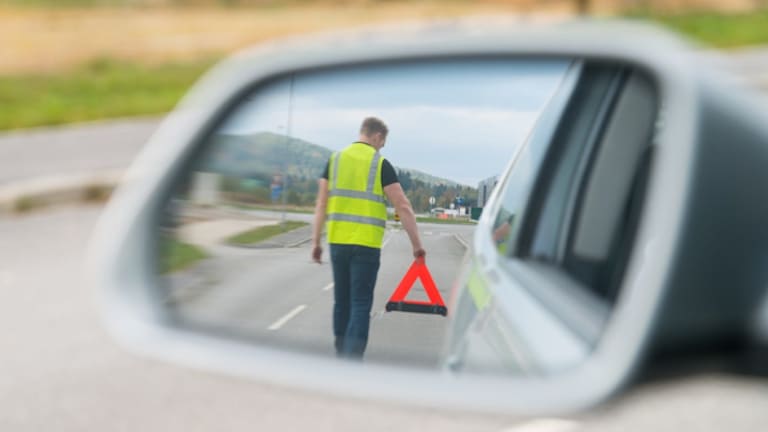 Conductor amb armilla reflectant homologada posant el triangle d'emergència